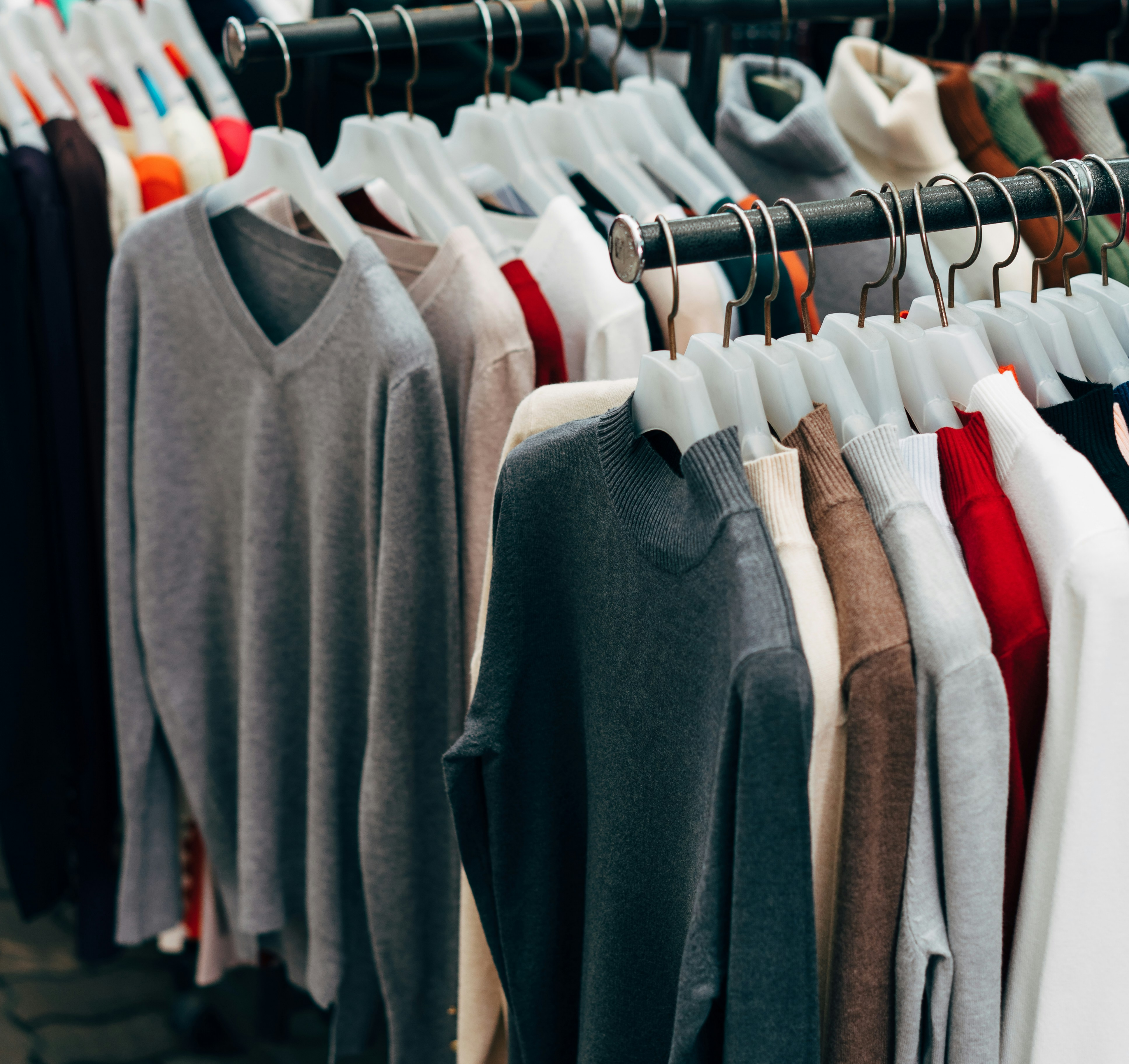 Rows of various knitted sweaters and tops hanging neatly on hangers along apparel display racks at a clothing market.