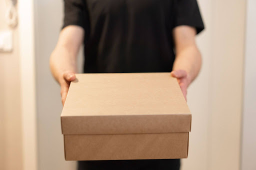 A delivery person holding out a plain, unbranded cardboard box for an EPROLO white label dropshipping package fulfillment.