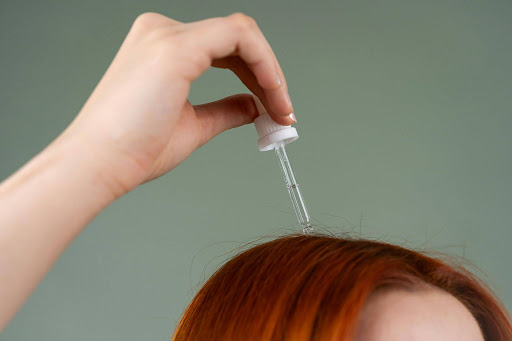 A person applying essential liquid serum directly onto their scalp using a glass dropper, showcasing a trending EPROLO viral hair wellness routine.