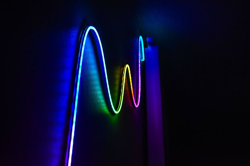 A flexible RGB LED neon strip light glowing in vibrant wavy patterns against a dark wall, showcasing an EPROLO lightweight smart home deco product.