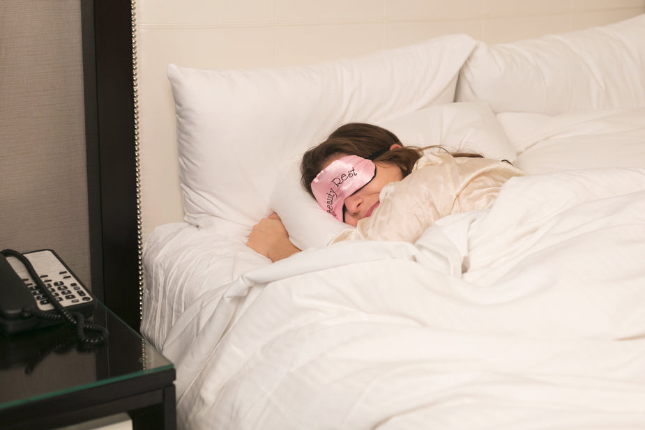 A woman sleeping peacefully in a comfortable bed while wearing a pink satin eye mask, highlighting top EPROLO mental health products to dropship for relaxation and wellness.