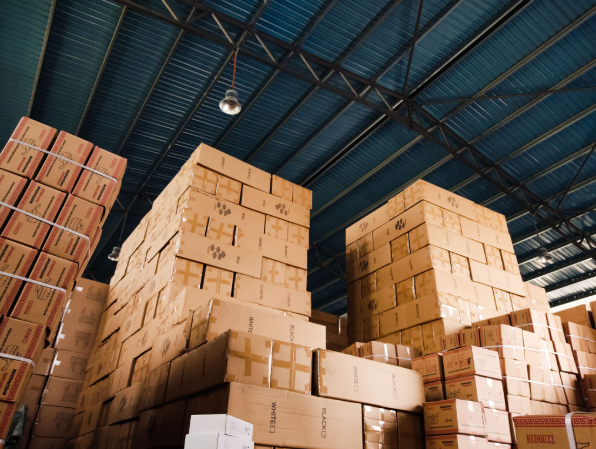 Massive stacks of sealed cardboard boxes piled high toward a blue metal ceiling inside a bustling fulfillment center, illustrating warehouse storage scale when transitioning from AliExpress to EPROLO dropshipping.