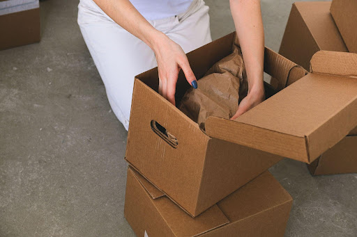 A warehouse worker carefully packing brown protective paper into a cardboard shipping box on the floor, illustrating efficient package handling for EPROLO fast shipping for dropshipping.
