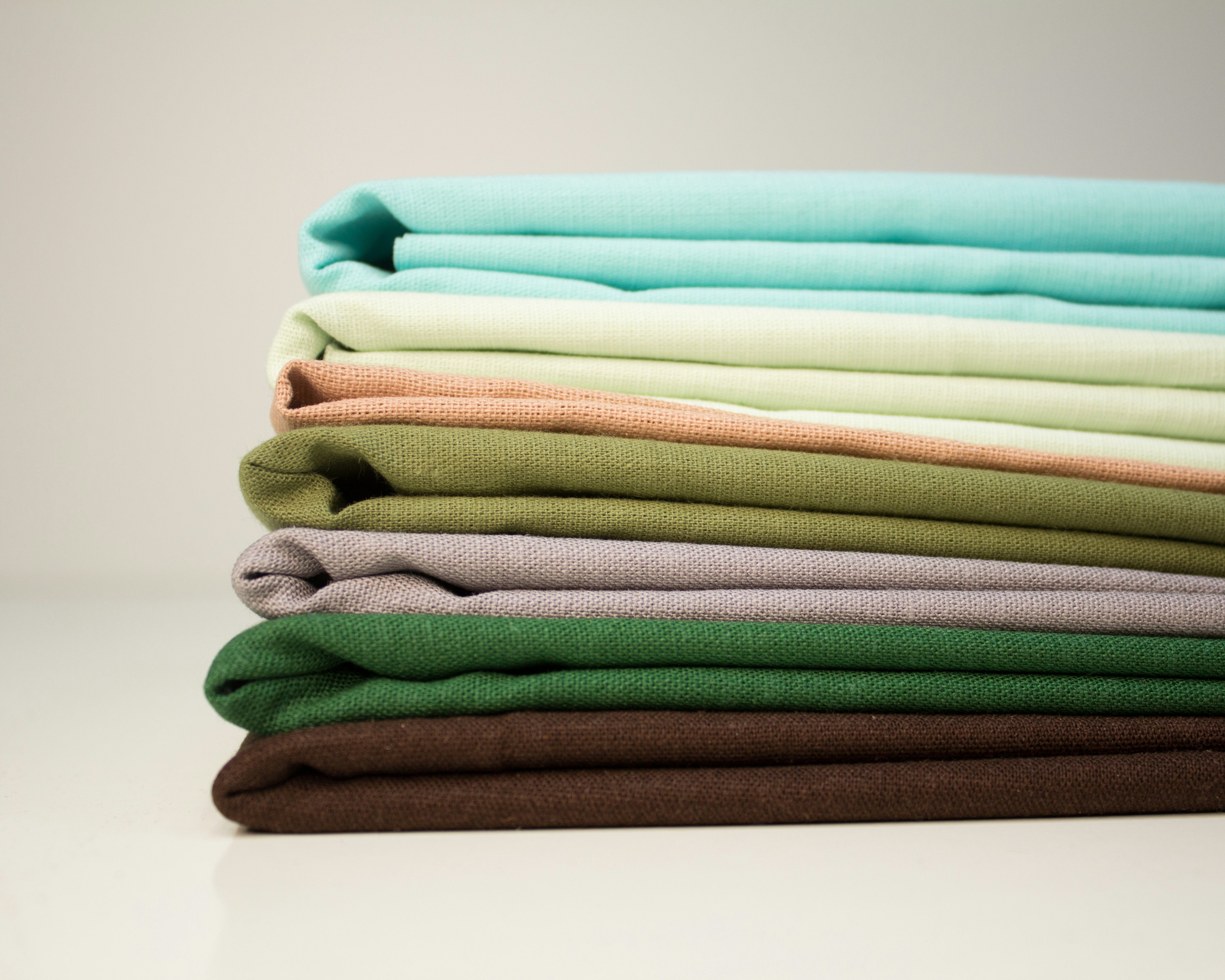 A stack of neatly folded fabrics in various earth-toned and pastel colors, showcasing material selection options for an EPROLO fashion dropshipping store.