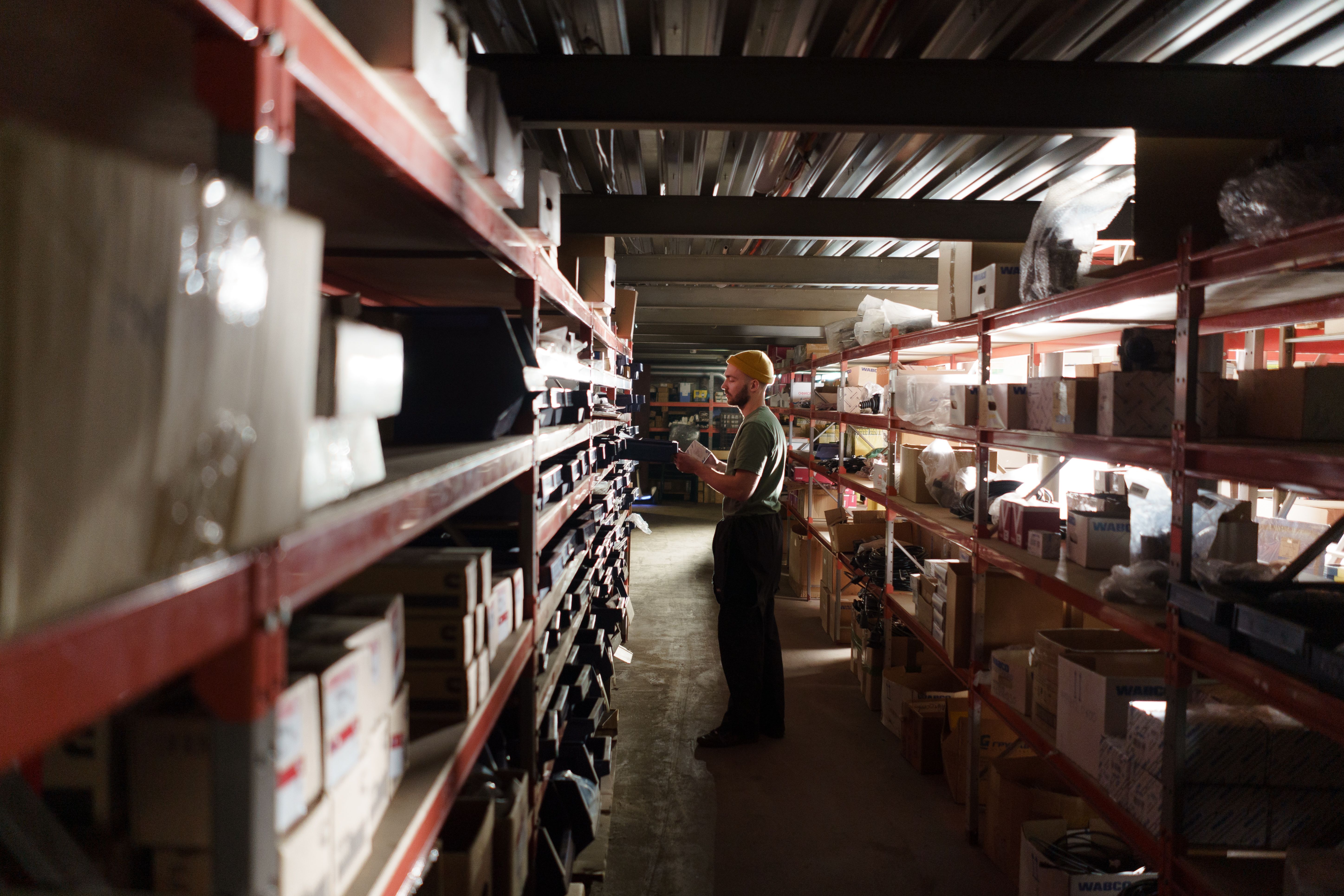 A warehouse worker inspecting inventory items along long storage shelves to fulfill individual orders, illustrating the flexible fulfillment process provided by EPROLO dropshipping suppliers no moq.