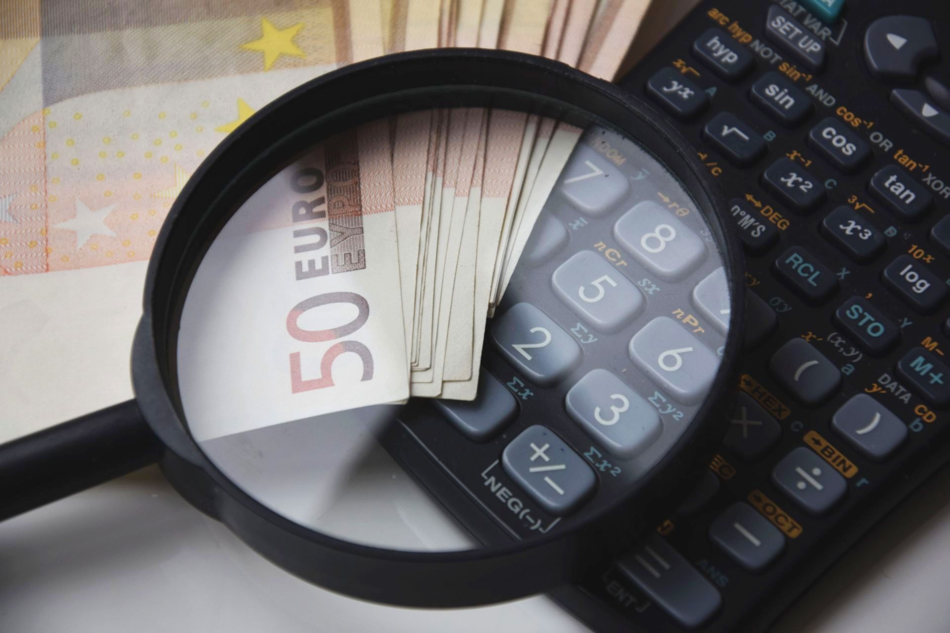 A magnifying glass closely scrutinizing a stack of Euro banknotes next to a calculator, illustrating the precise financial audit required to detect EPROLO hidden sourcing fees.