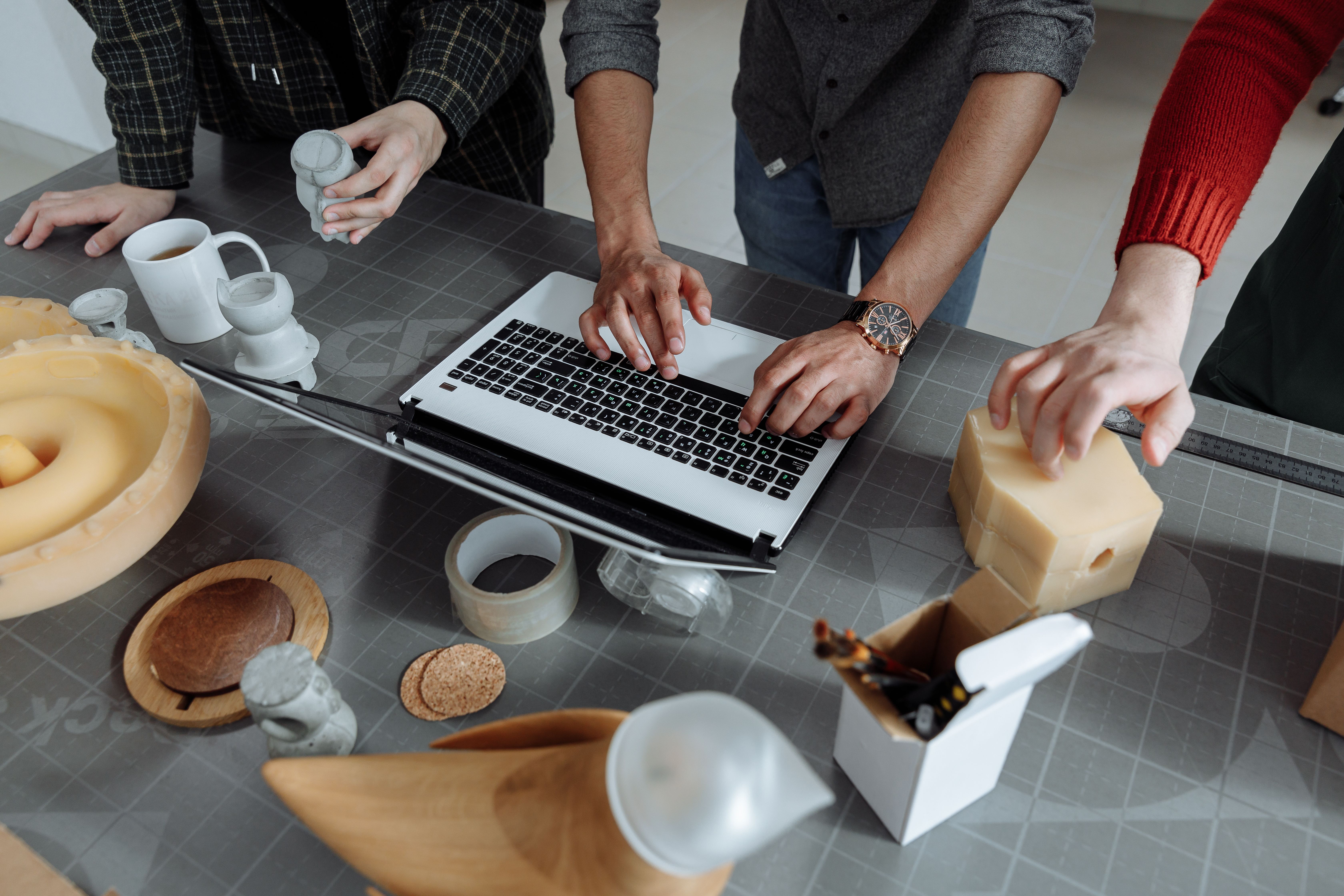 An entrepreneur typing on a laptop while collaborating with team members handling product components at a workspace desk, illustrating cross-border planning for the EPROLO EU €150 exemption removed regulatory update.