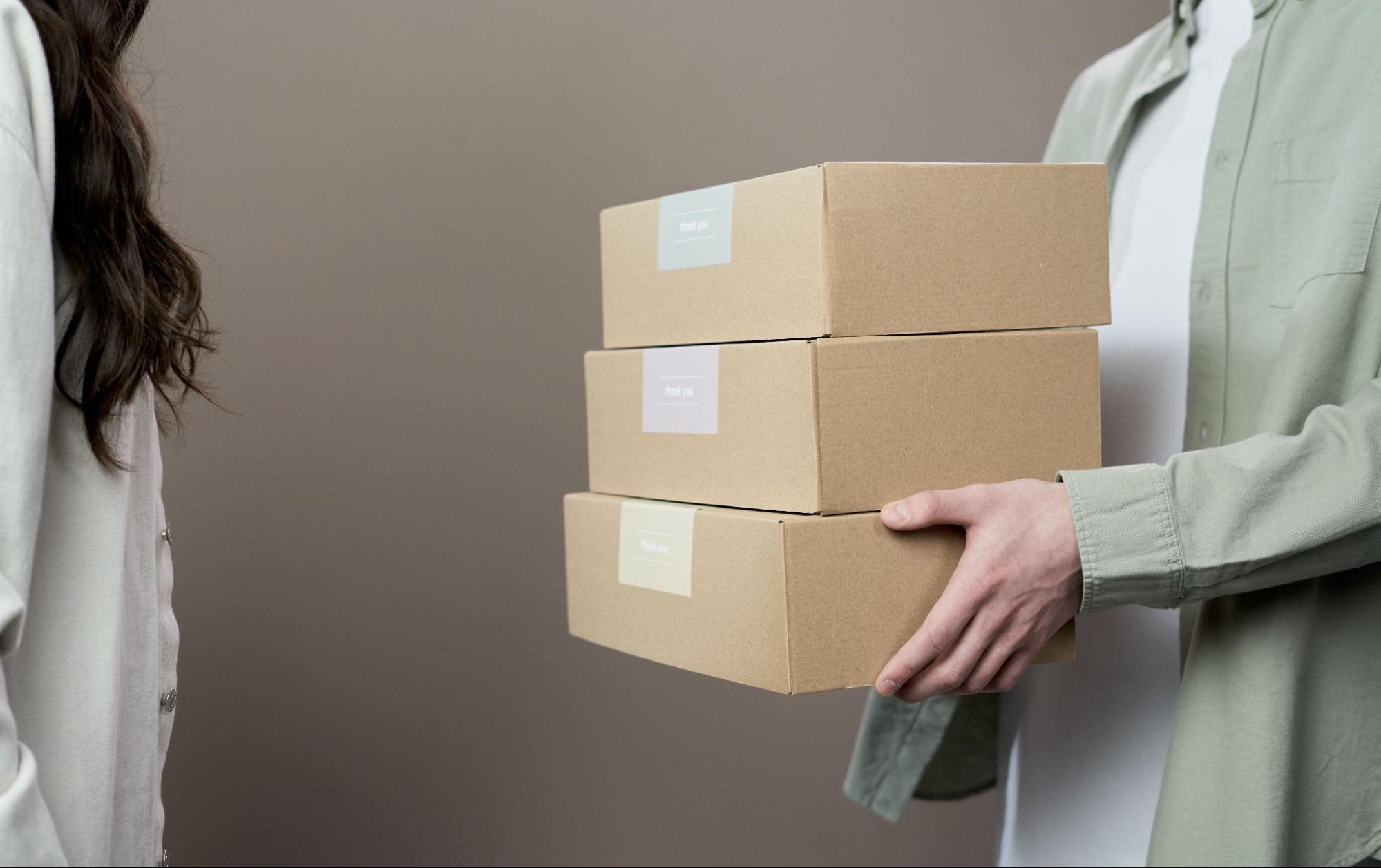 A person handing a stack of cardboard boxes to a customer for custom packaging dropshipping with EPROLO.