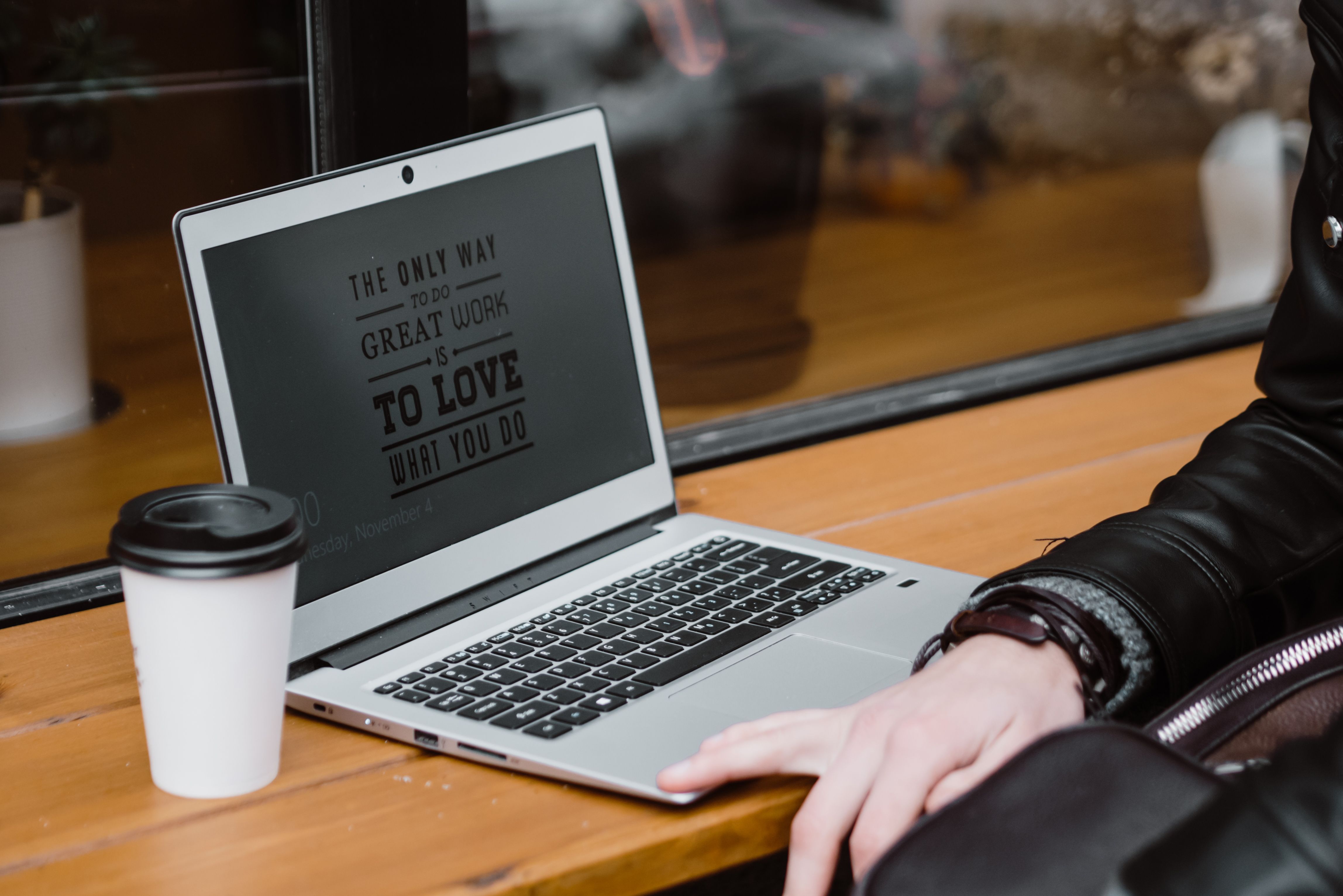 A person working on a laptop displaying motivational quotes beside a cup of coffee.