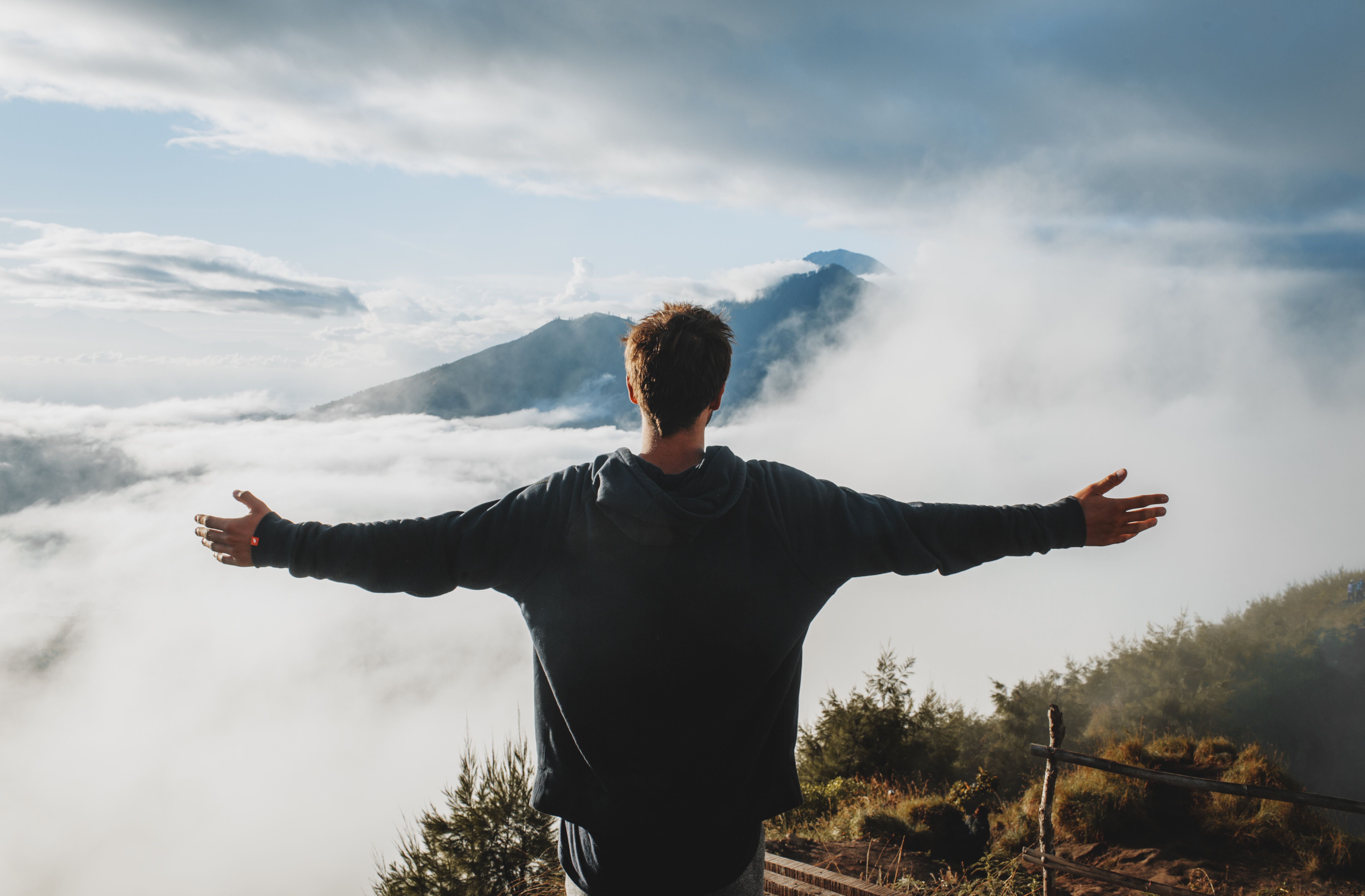 A man standing with open arms above mountain clouds, reflecting meaningful quotes about life.