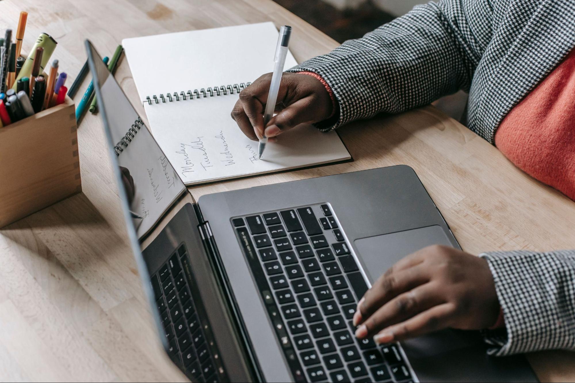 A person typing on a laptop and taking notes to start a small business.