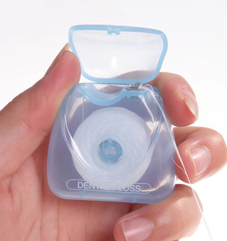 Compact egg-shaped dental floss dispenser held in hand against a soft cream background, demonstrating easy one-handed use