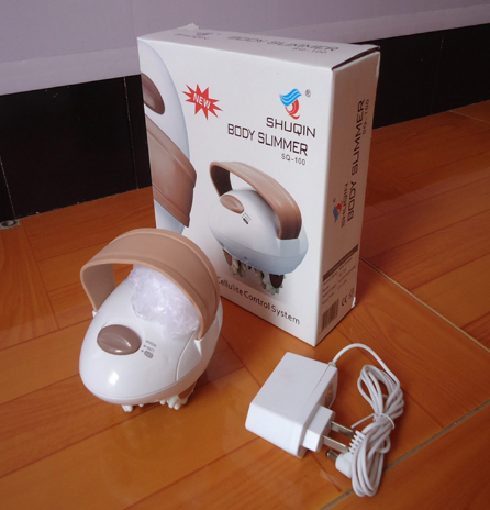 The 3D massager unboxed, showing white device with taupe accents and multiple attachments on a light wood table