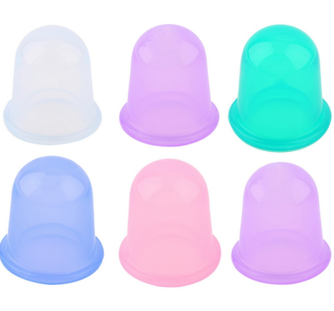 Six pastel silicone cupping cups arranged in two rows on warm travertine, eucalyptus accent, overhead view