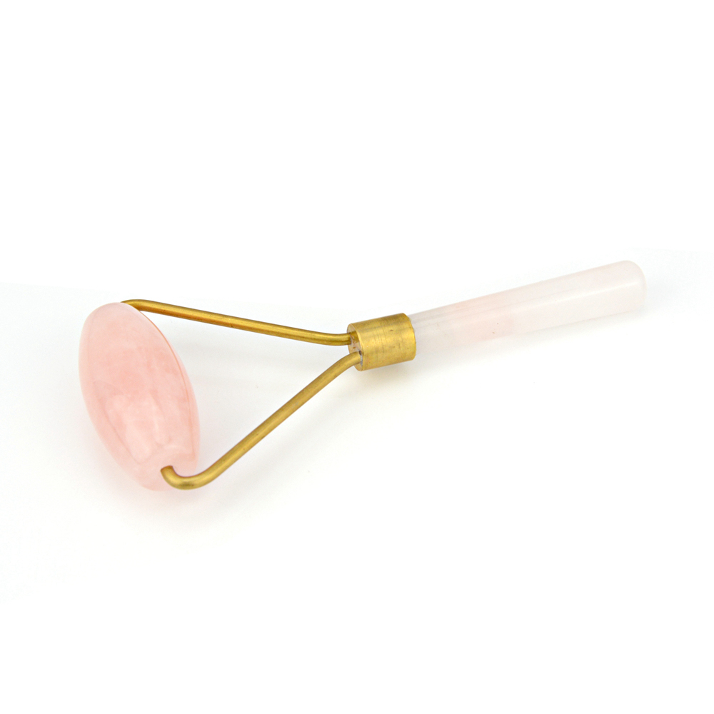Angled close‑up of flat massage stone showing natural rose quartz texture and brass handle detail