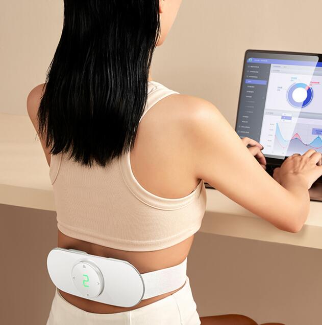 Woman at desk wearing waist massager while using smartphone app to adjust intensity and track progress