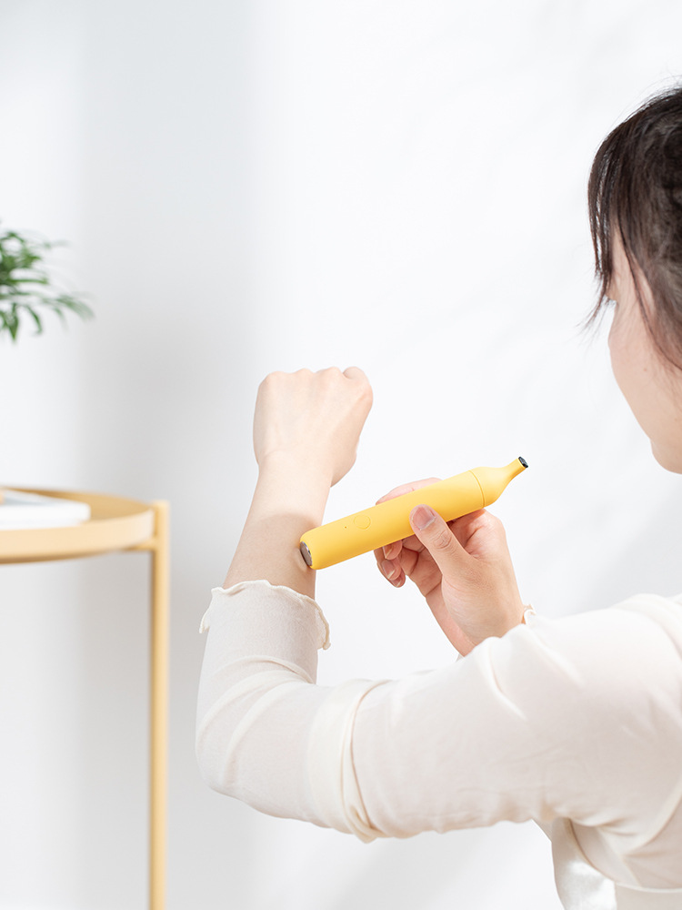 Close-up of the yellow banana anti-itch pen with touch button visible, held by a woman in a white sweater