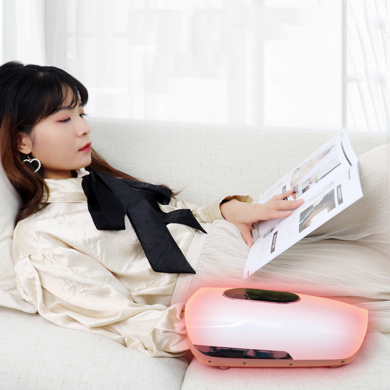 Woman relaxing on couch using pink hand massager while reading, demonstrating leisure use