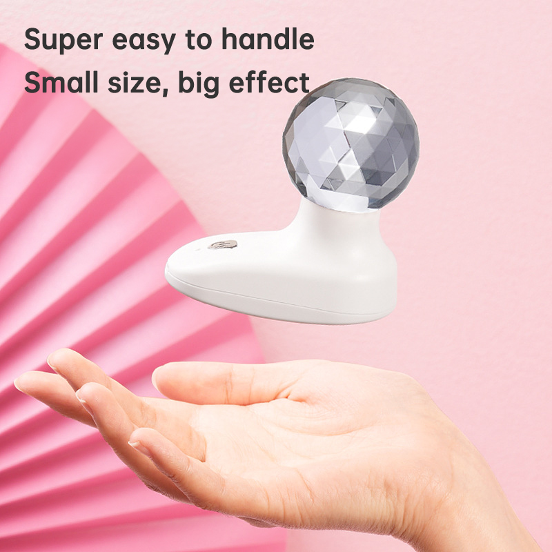 Hand holding compact white fascia gun with crystal head against pink gradient backdrop