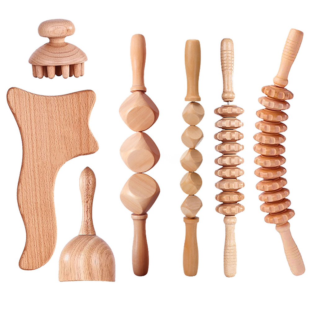 Complete wooden massage tool set arranged on a pale celadon ceramic surface, featuring gua sha cups, beaded roller, scraper, and comb-like massager