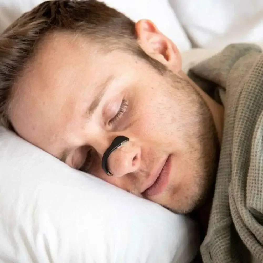 Man peacefully sleeping on white pillow with black nasal dilator clip in place, relaxed expression