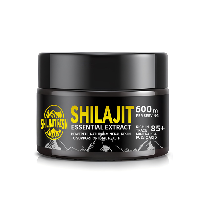 Dark glass shilajit jar with gold and silver branding on a soft lilac acrylic surface, sharp focus with dramatic tilt