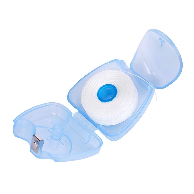 Opened egg-shaped case showing the 50m floss spool and built-in metal cutter, bathed in soft natural light with a chamomile flower accent