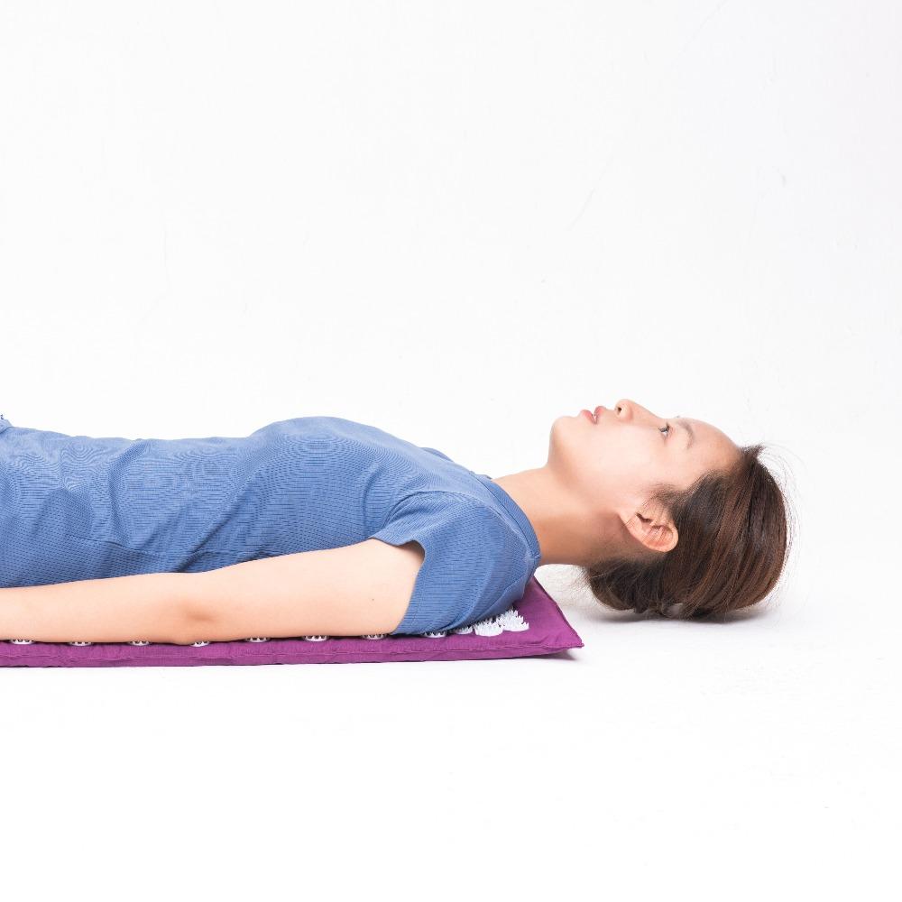 Woman lying on purple acupressure mat visibly relaxed with eyes closed