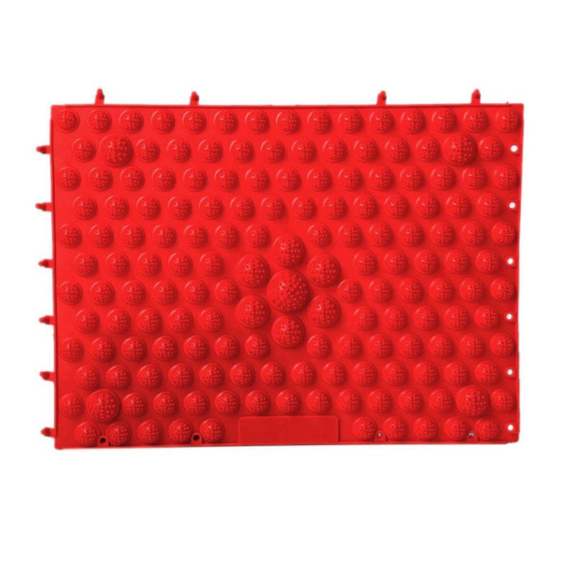 Bright red reflexology foot massage pad with raised spherical acupressure nodules on pale honey-oak wood surface