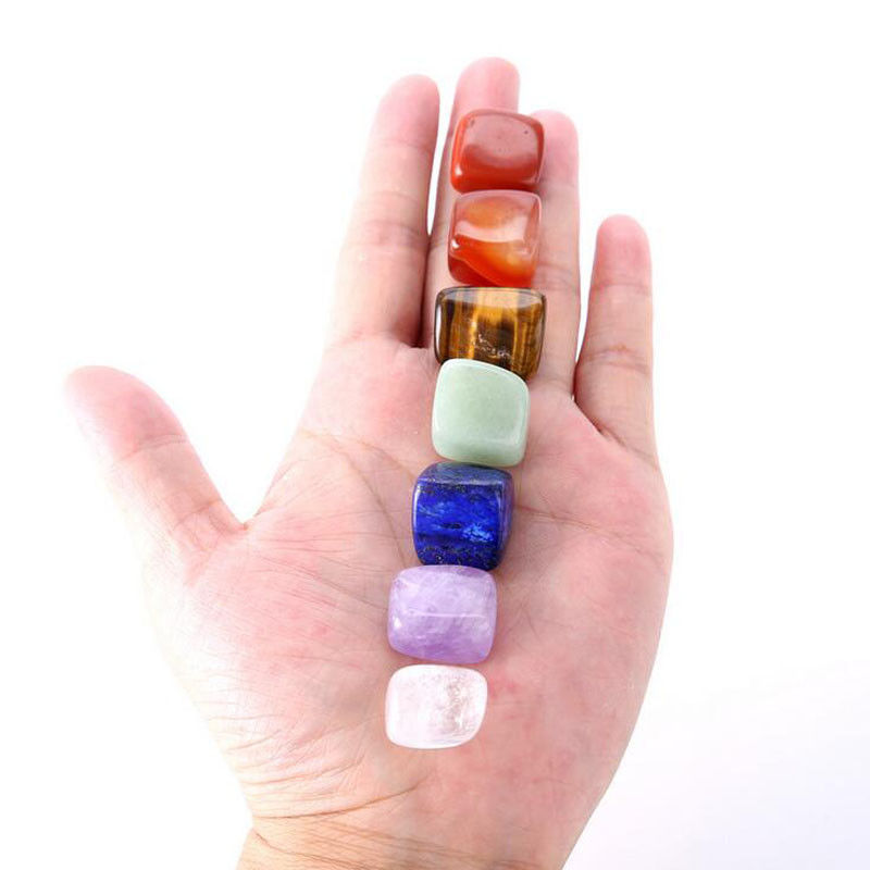 Seven chakra stones lined up across an open palm showing compact size and rainbow colors