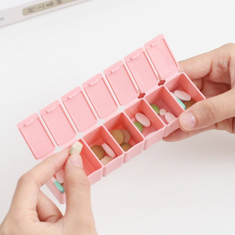 Hands opening the pink pill organizer revealing multiple compartments filled with various tablets and capsules