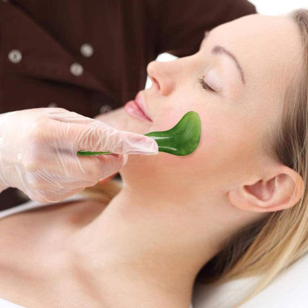 Professional spa treatment of woman receiving facial gua sha massage with jade tool on jawline