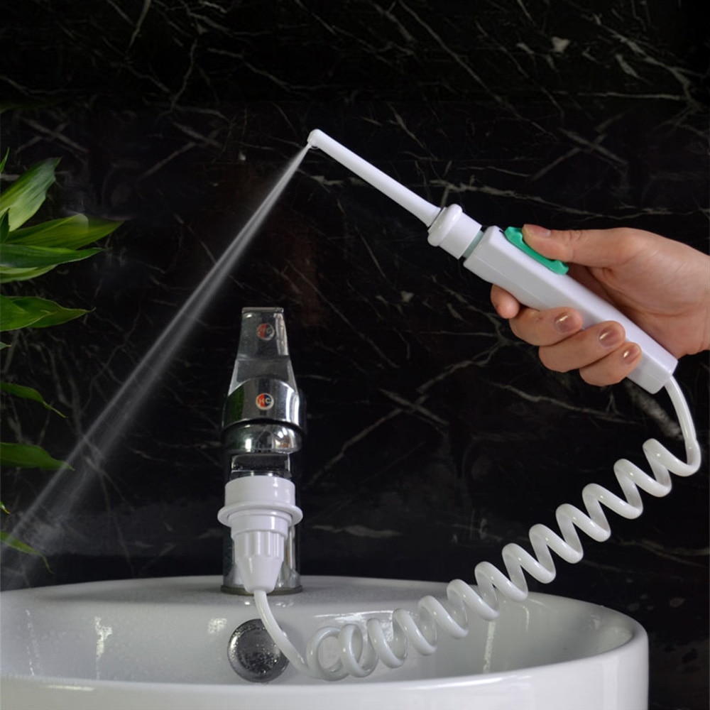 Water flosser in use at a bathroom sink, hand holding white device with teal nozzle, water spray dispersing