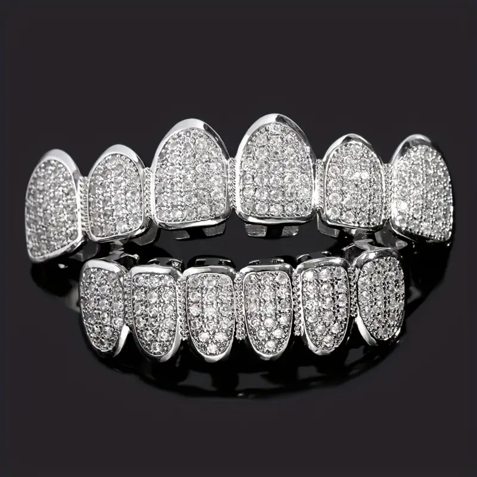 Silver-tone CZ grillz top and bottom set laid flat on dark reflective surface, dense micro-pavé diamond coverage