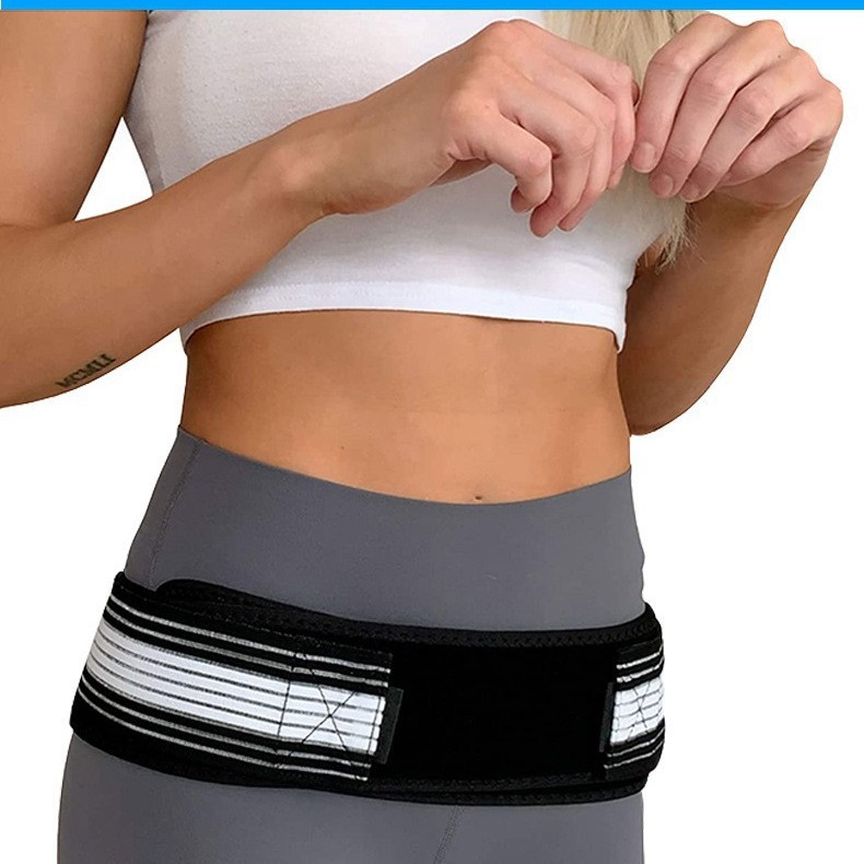 Woman wearing white crop top and gray waistband with black mesh hip cinch belt, hands adjusting fit, showing visible waist cinching and hip lifting effect