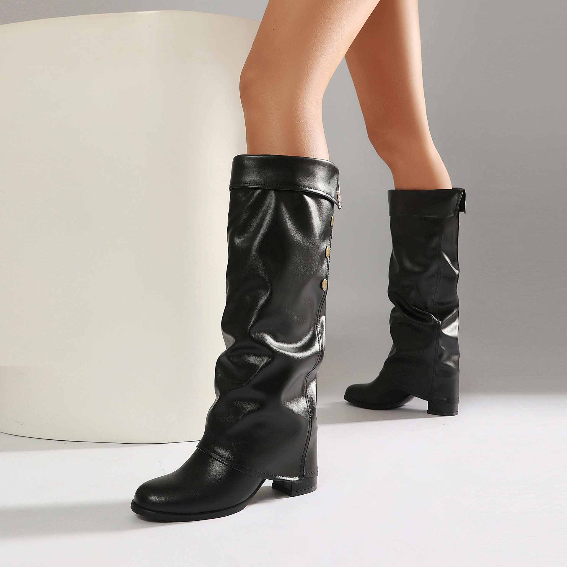 Black knee-high boots – close-up of fold-over cuff with gold stud detail and logo hardware